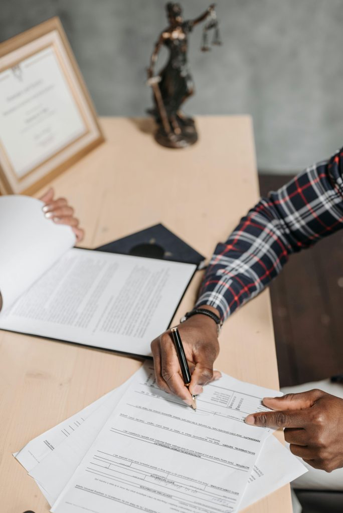 pexels-photo-8152746-8152746 Hands of a person signing official documents on a desk in an office setting.